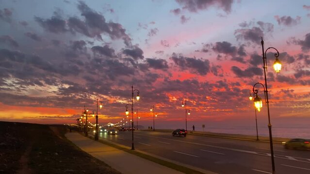 Rabat coastal road car traffic by the ocean during mesmerizing dusk sky with reddish sun reflections on scattered clouds after sunset