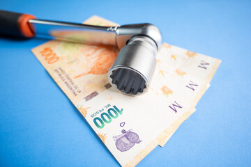Argentine pesos tightened by a ratchet wrench on a blue background.