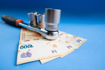 Concept of the cost of mechanics made with a ratchet wrench and Argentine peso bills on a blue...