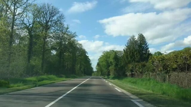 Country road in France from car front window, dashboard view on read and surrounding landscape, driving ahead, trees, woods on both sides