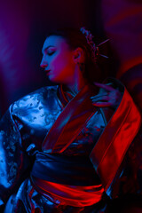 A beautiful girl in a kimono lies in colored light. The image of a geisha, Chinese national costume. Party concept, night club