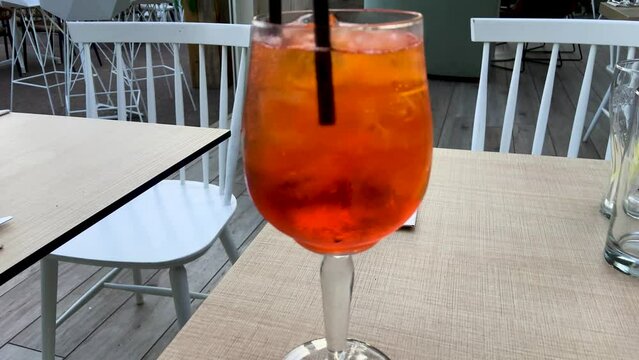 Orange citrus alcohol drink with fruit slices, ice cubes and straw on the cafe table on a sunny summer day, mixing cocktail ingredients in wine glass