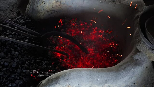 A piece of bronze is being burned on burning coal in a factory. A traditional copper and brass household appliance factory.