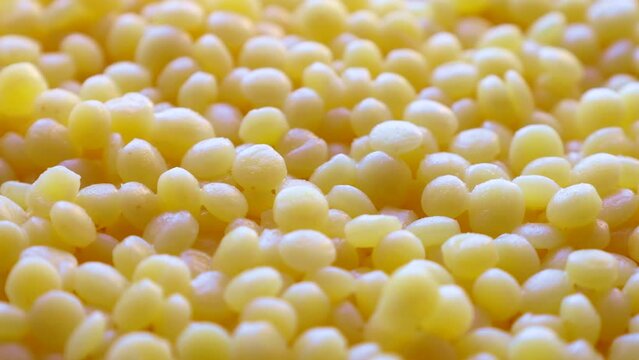 Yellow cooked wheat ptitim pasta groats (pearl or Israeli couscous) circle rotation close up