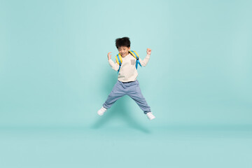 Fototapeta na wymiar Asian little boy jumping and carries a backpack to school in casual clothes isolated on green background, Back to school concept
