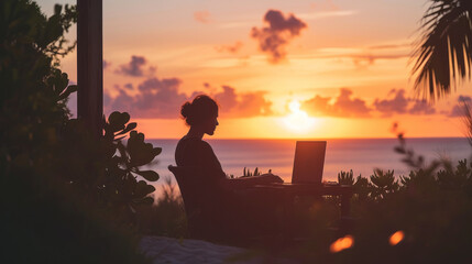 Woman remote working at laptop in front of ocean at sunset