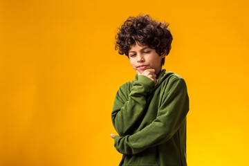 Thoughtful child boy holds chin on yellow background. Dreaming concept - obrazy, fototapety, plakaty