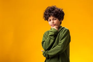 Poster Thoughtful child boy holds chin on yellow background. Dreaming concept © Aleksej