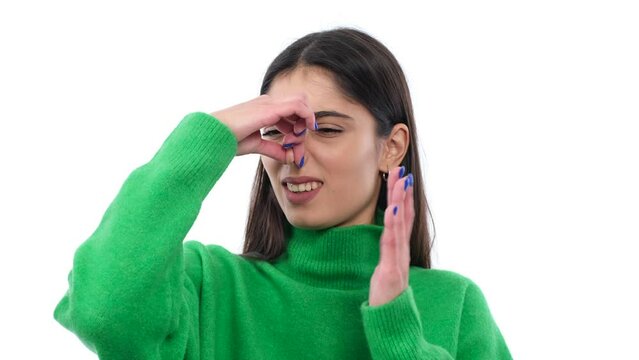 Displeased, annoyed young Caucasian woman covering nose from a stinky, nasty odor over white background. Bad scent, unclean air concept.