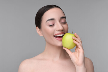 Beautiful young woman with apple on grey background