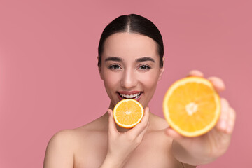 Beautiful young woman with pieces of orange on pink background, selective focus