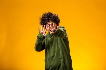 Afraid child boy showing stop gesture on yellow background. Bulling and negative emotions concept