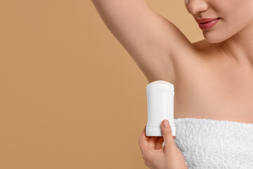 Woman applying deodorant on beige background, closeup. Space for text