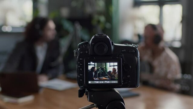 Selective focus of video camera on tripod recording online show with interviewing musician with guitar in studio
