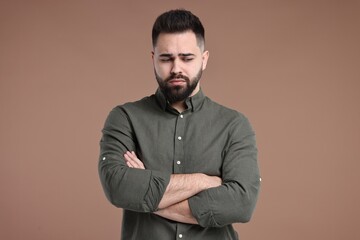 Obraz premium Portrait of sad man with crossed arms on brown background