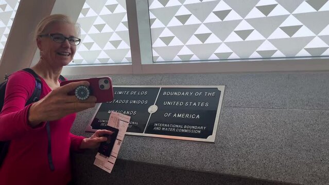 Woman taking a selfie of her in front of the Mexico USA border in the Cross Border Xpress bridge linking San Diego with Tijuana airport.