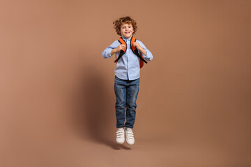 Happy schoolboy with backpack jumping on brown background