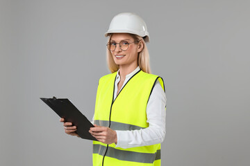 Engineer in hard hat holding clipboard on grey background