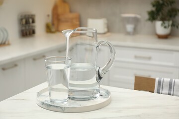 Fototapeta na wymiar Jug and glass with clear water on white table in kitchen