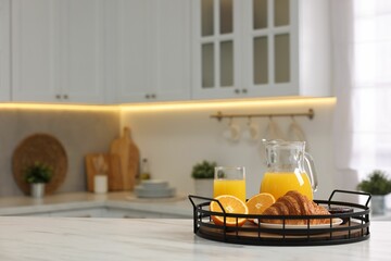 Breakfast served in kitchen. Tray with fresh croissant, jam and orange juice on white table, space for text