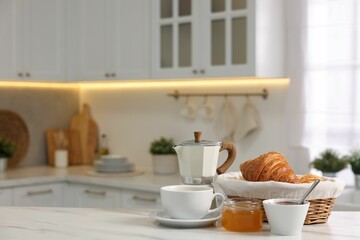 Breakfast served in kitchen. Fresh croissants, jam, honey and coffee on white table, space for text