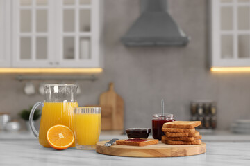Breakfast served in kitchen. Crunchy toasts, jam and orange fresh on white table