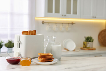 Making toasts for breakfast. Appliance, crunchy bread, honey, jam and milk on white marble table in kitchen. Space for text