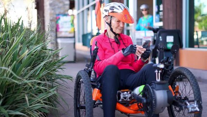Elderly woman on recumbent e bike electric bicycle checking messages on phone, scrolling, looking at map navigation. - Powered by Adobe