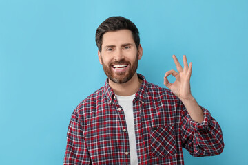 Portrait of smiling man with healthy clean teeth showing ok gesture on light blue background