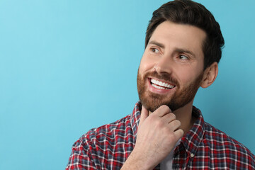 Portrait of smiling man with healthy clean teeth on light blue background. Space for text