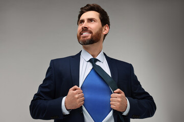 Happy businessman wearing superhero costume under suit on beige background