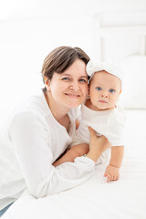 mom gently hugs her baby daughter kissing and admiring them, happy family, mom with baby on the bed, maternal love and care, mom on maternity leave playing with the baby