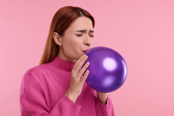Woman inflating purple balloon on pink background