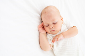 cute little newborn baby sleeps with his hand folded under his cheek, sweet healthy baby sleep in a white crib, a place for text