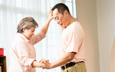 Fototapeta premium Asian sweet senior elderly couple wearing casual clothes, staying in indoor cozy home at living room, dancing together with happiness and passion, smiling. Retirement, Lifestyle, Healthcare Concept.