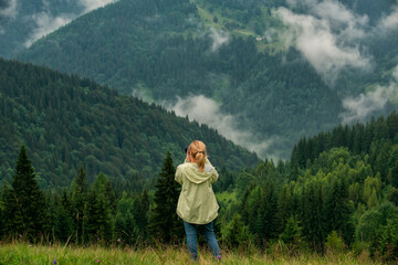 Fototapeta na wymiar A girl tourist photographs a foggy mountain landscape.