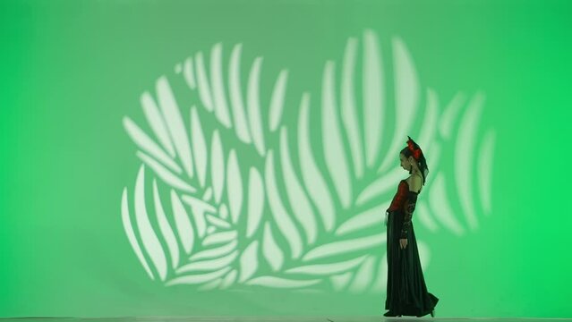 Woman dancer dancing on green background. Female in flamenco style dress performs elegant spanish dance moves with her hands and body in the studio.