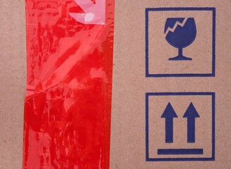 Two signs on cardboard box - Fragile and This Way Up and a red scotch tape on a cardboard