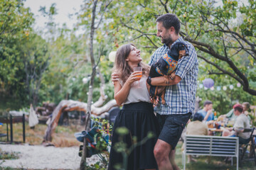Naklejka na ściany i meble Young attractive romantic happy Caucasian couple with their pet dachshund dog spending time together during a garden party. Love concept