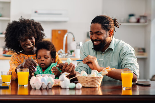 Portrait of an interracial family sits at home and colors easter eggs.