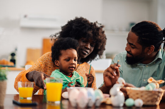 African american parents teaching happy little kid son to decorate ester eggs