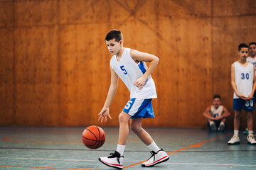 A basketball young athlete is dribbling a ball on court on training.