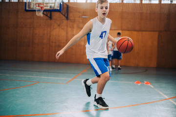 Naklejka premium A young basketball kid in action dribbling a ball on court on training.