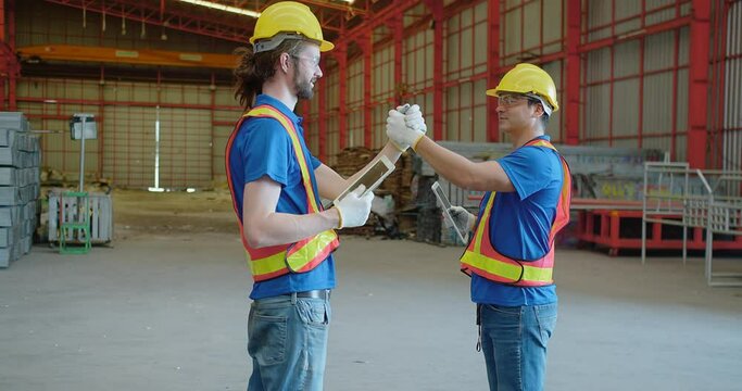 Two construction engineer workers in hard hats and vests engage in a friendly arm wrestling on a construction site, giving each other a fist bump blending teamwork with a light-hearted moment