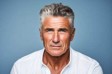 Portrait of mature man with grey hair looking at camera against blue background