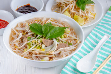A delectable serving of Vietnamese Beef Ball Pho, accompanied by a selection of sauces and a side of fresh sprout beans.