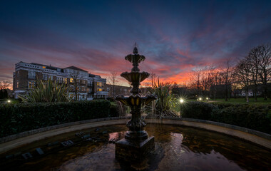 Fountain and pond in a park at sunset with a pink sky. Dusk view in landscape orientation with...