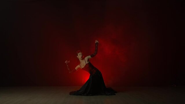 Woman dancing on black background with red light and smoke. Spanish dancer in red and black dress demonstrates elements of flamenco choreography.