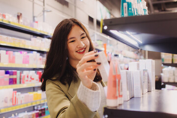 Young girl holds a bottle of cream in her hands in retail store. Beautiful woman testing and buying cosmetics in a beauty store. Side view. Personal care and modern cosmetology