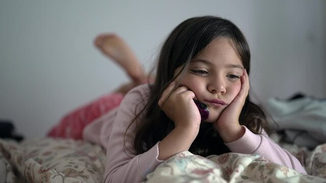 One bored little girl feeling extreme boredom with nothing to do laid in bed with hands in chin. Sad contemplative 8 year old child close-up face